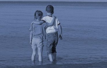 A sister and brother paddling in the sea with arms around each other
